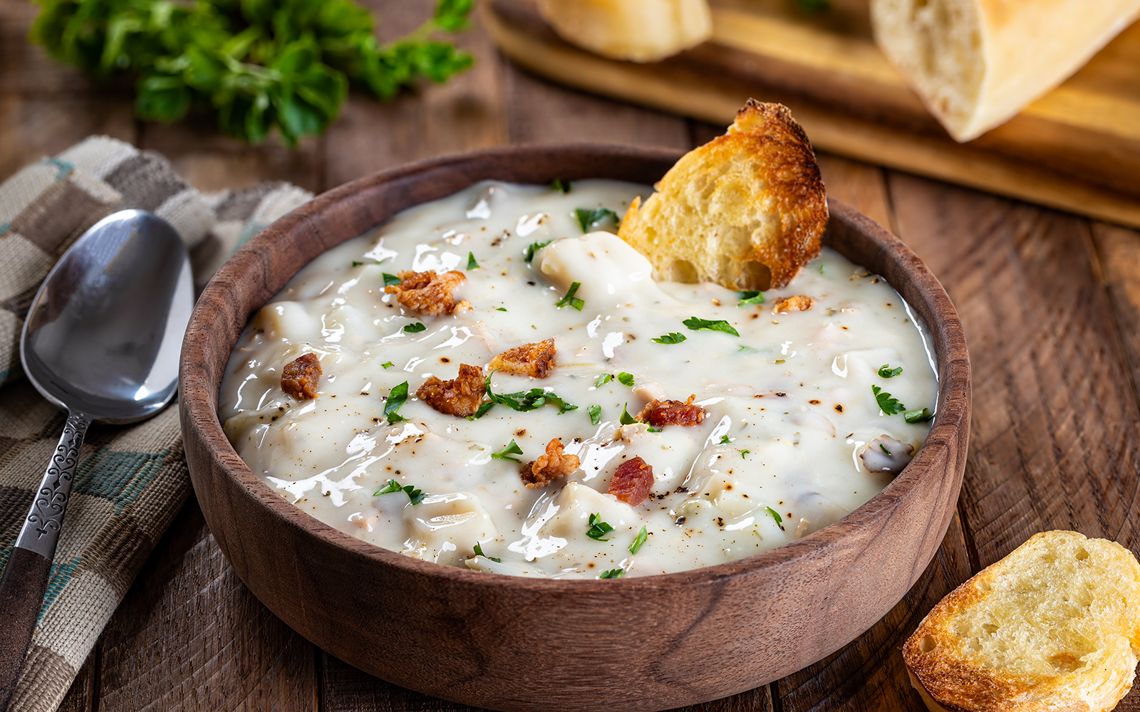Clam chowder in a wooden bowl with bread and herbs, New England cuisine.