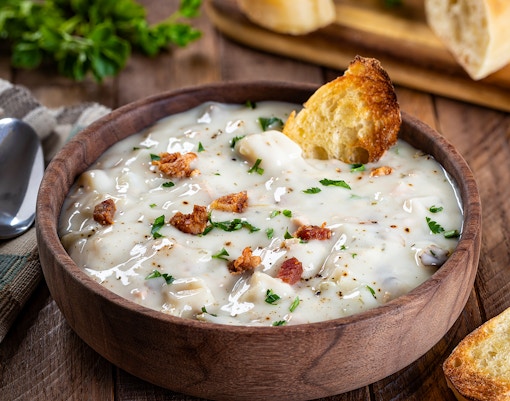 Clam chowder in a wooden bowl with bread and herbs, New England cuisine.