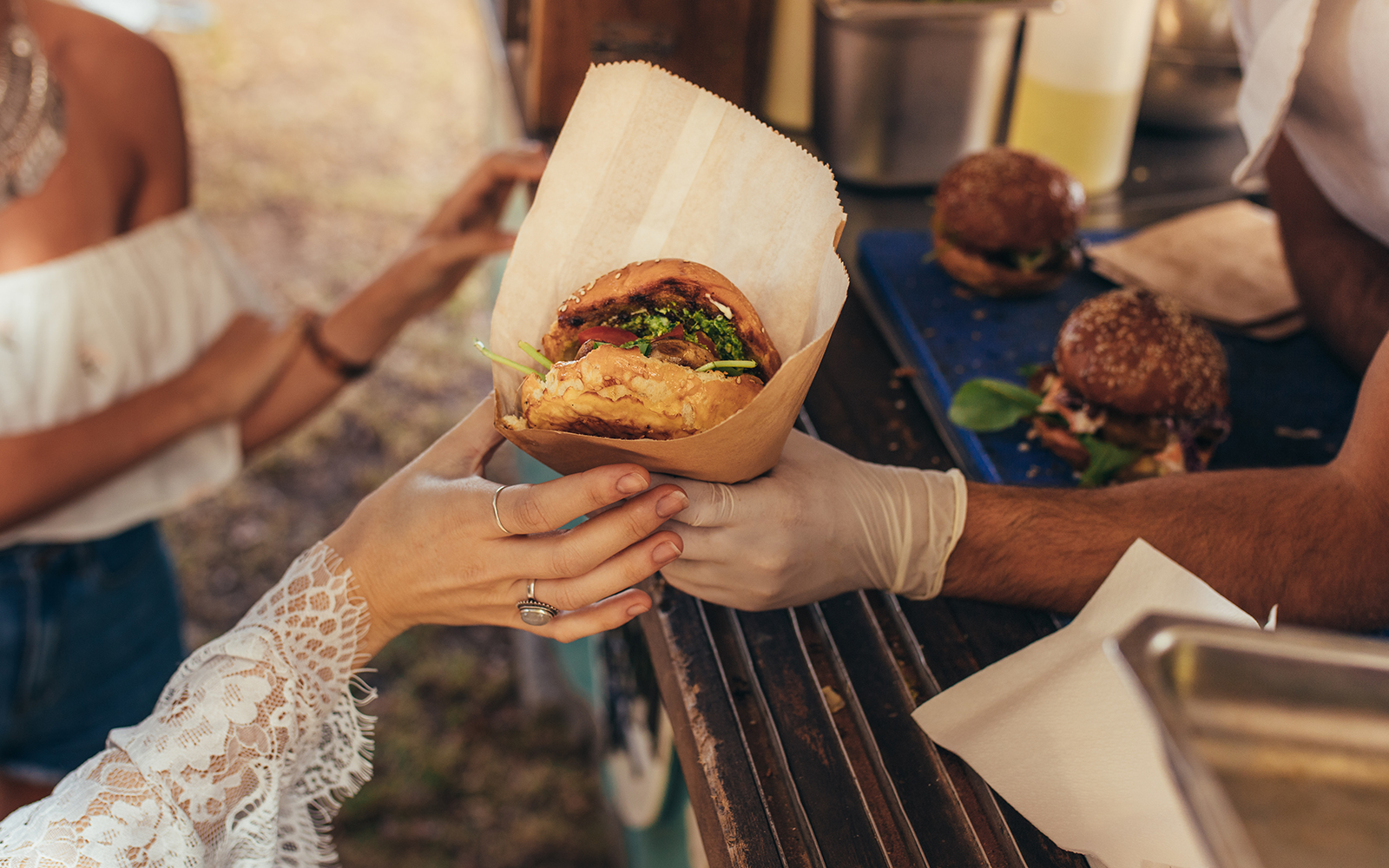 Street food vendor handing a burger to a customer at an outdoor market.