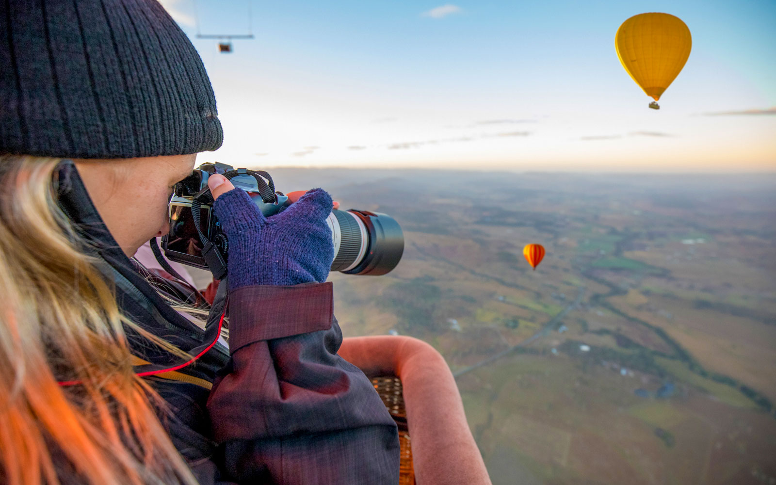 Person photographing hot air balloons over Brisbane landscape.