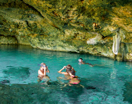 Tourists snorkeling in a cenote, Yucatan Peninsula, Mexico, surrounded by limestone formations.