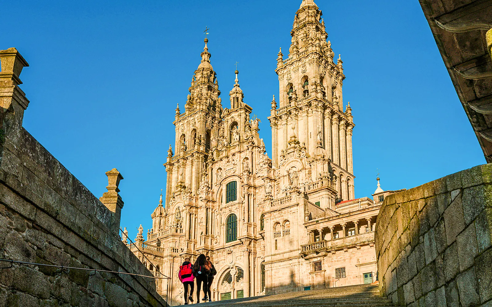 Santiago De Compostela Cathedral with visitors under a clear blue sky.