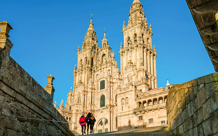 Santiago De Compostela Cathedral with visitors under a clear blue sky.