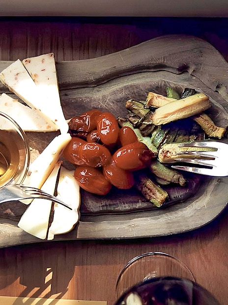 Cheese, tomatoes, and vegetables on a wooden platter during Chianti wine and olive oil tour.
