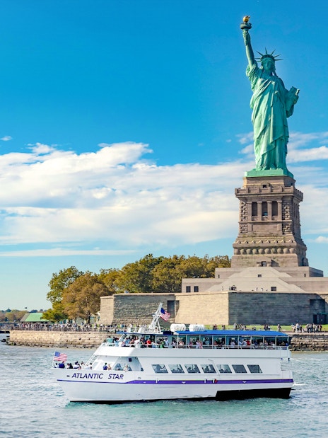 Tourists on a boat near the Statue of Liberty, New York, on a sunny day.