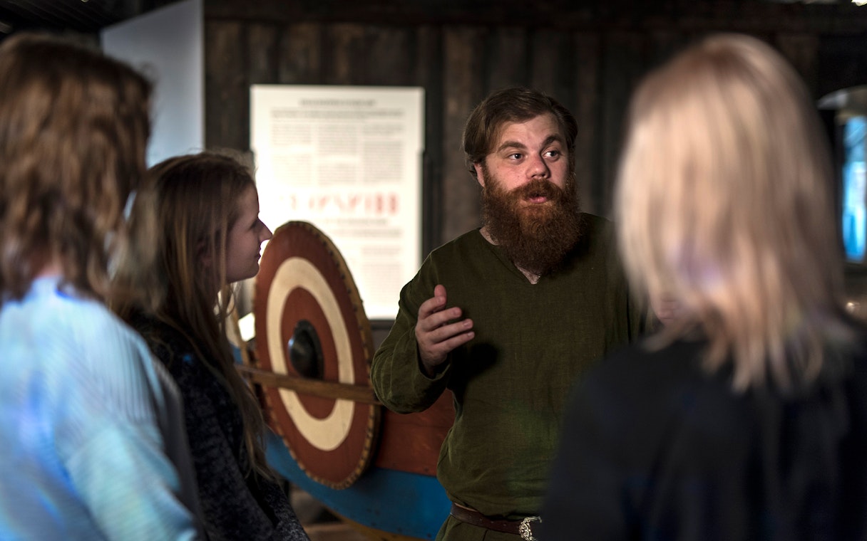 Guide explaining Viking history to visitors at Stockholm museum.