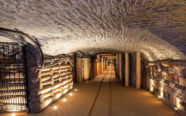 Underground corridor in Wieliczka Salt Mine with illuminated salt walls and wooden supports.