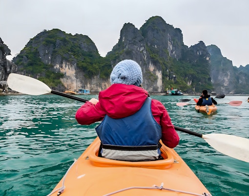 Kayakers paddling through Halong Bay's limestone cliffs on a Dragonfly Cruise tour.