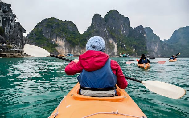 Kayakers paddling through Halong Bay's limestone cliffs on a Dragonfly Cruise tour.