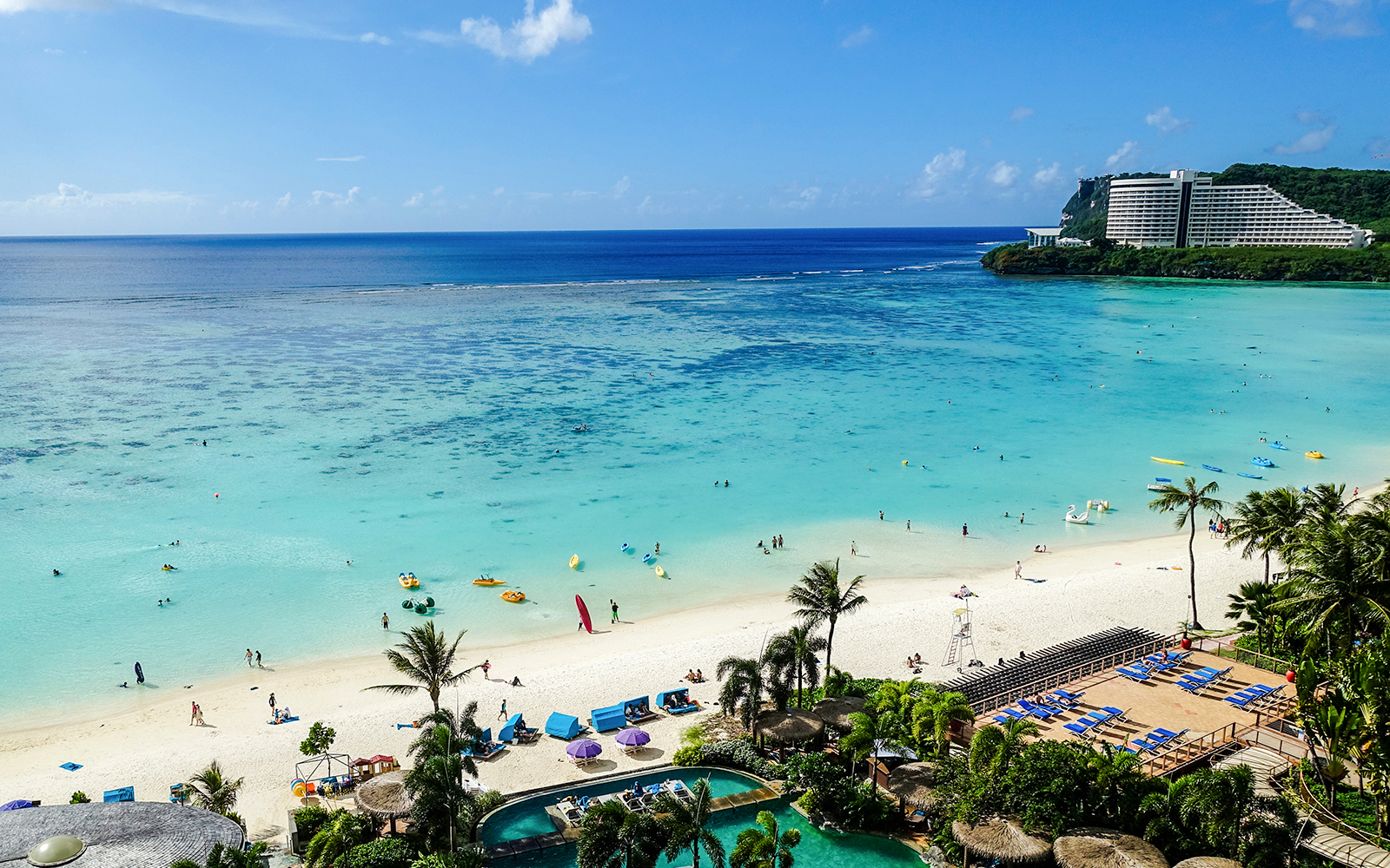 Tumon Bay Beach in Guam with clear blue waters and palm trees lining the sandy shore.
