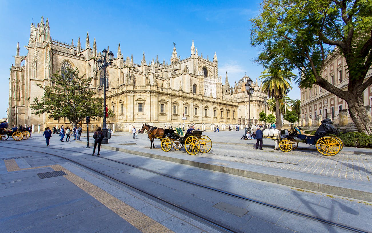 Seville Cathedral with horse-drawn carriages and tourists on a guided walking tour.