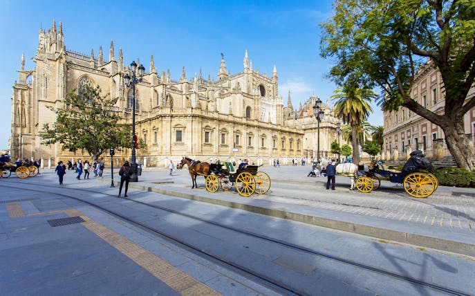 Seville Cathedral with horse-drawn carriages and tourists on a guided walking tour.