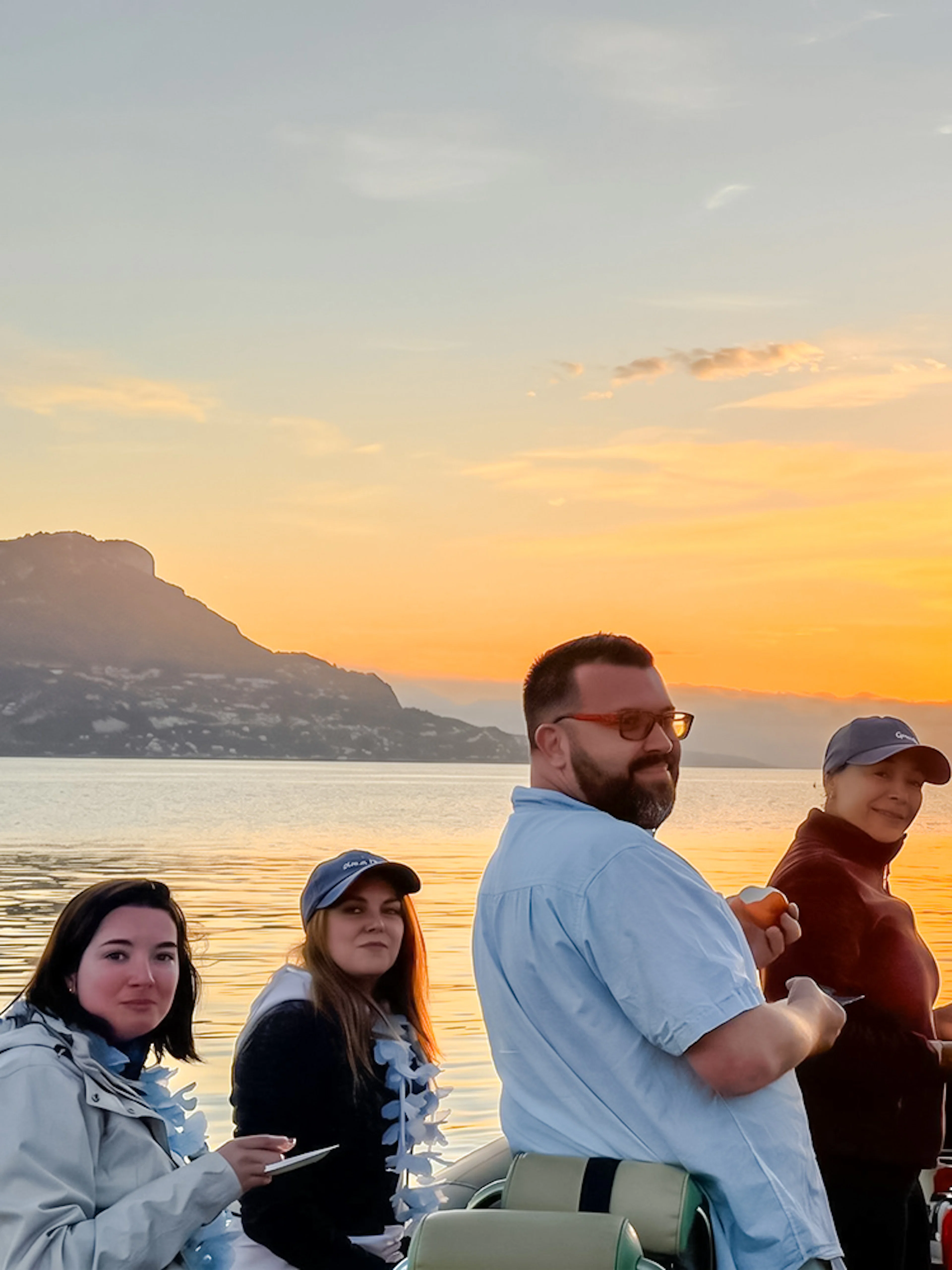 Group enjoying a sunset boat tour on a calm sea with mountains in the background.