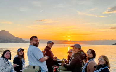 Group enjoying a sunset boat tour on a calm sea with mountains in the background.