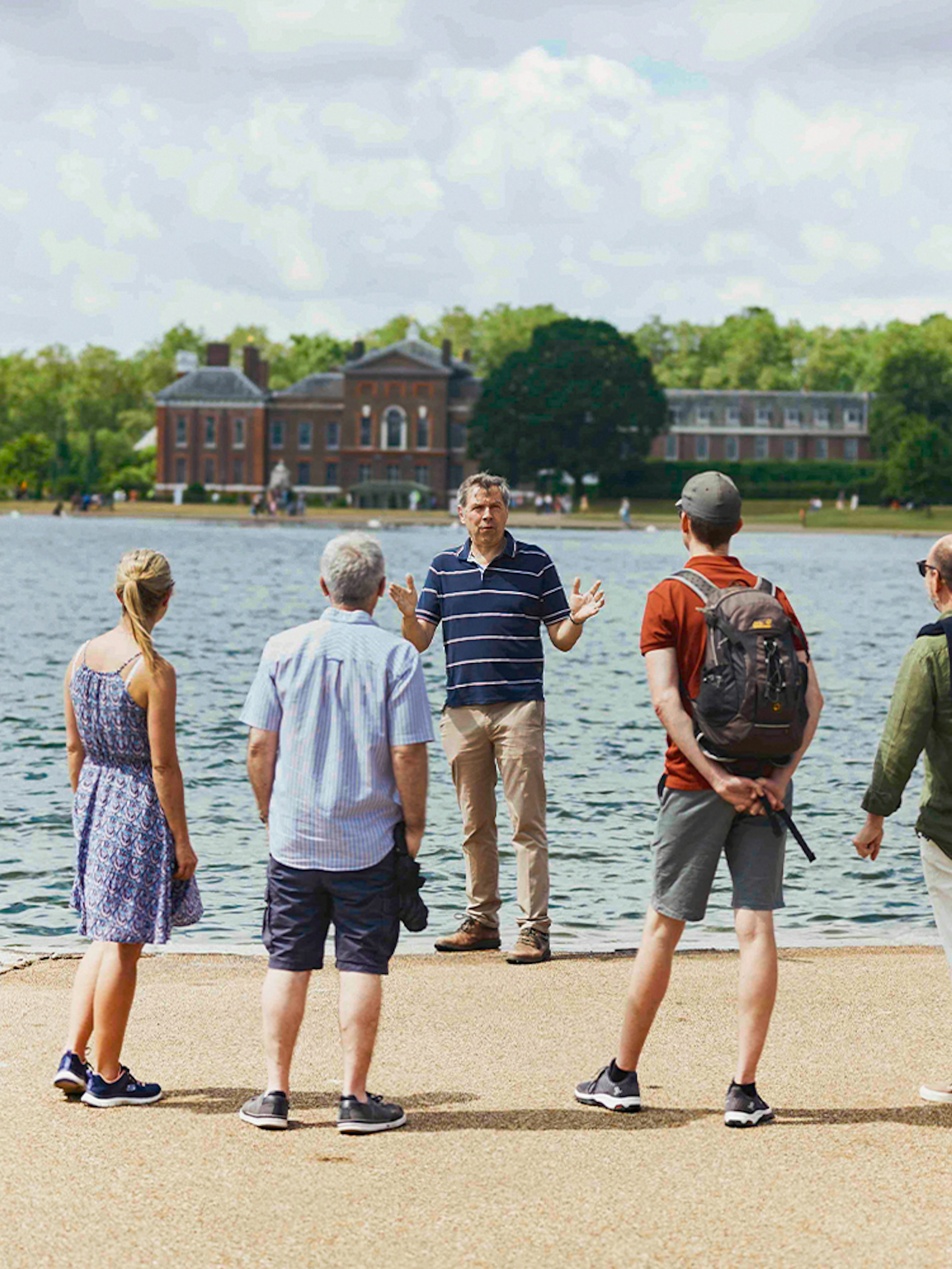 Tour group by Kensington Palace lake, listening to a guide during the Royal Afternoon Tea experience.