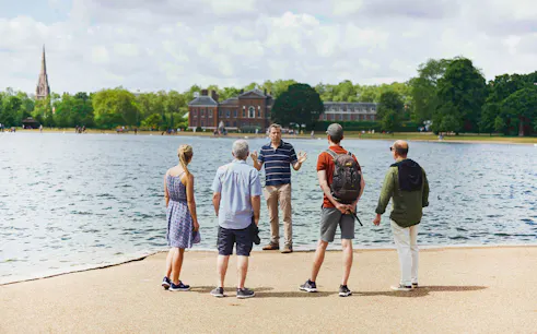 Tour group by Kensington Palace lake, listening to a guide during the Royal Afternoon Tea experience.