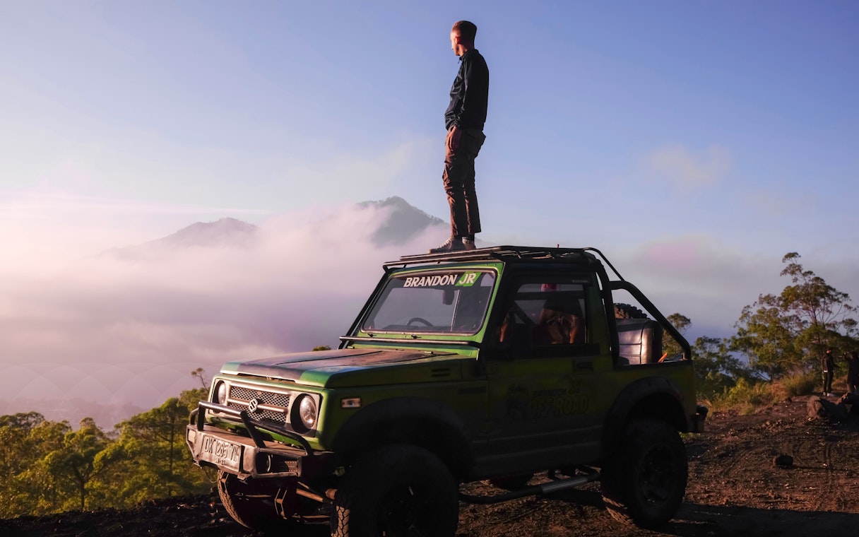 Man standing on a jeep during Black Lava Exploration in Bali with misty mountains in the background.