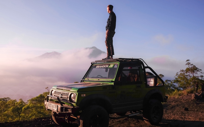 Man standing on a jeep during Black Lava Exploration in Bali with misty mountains in the background.