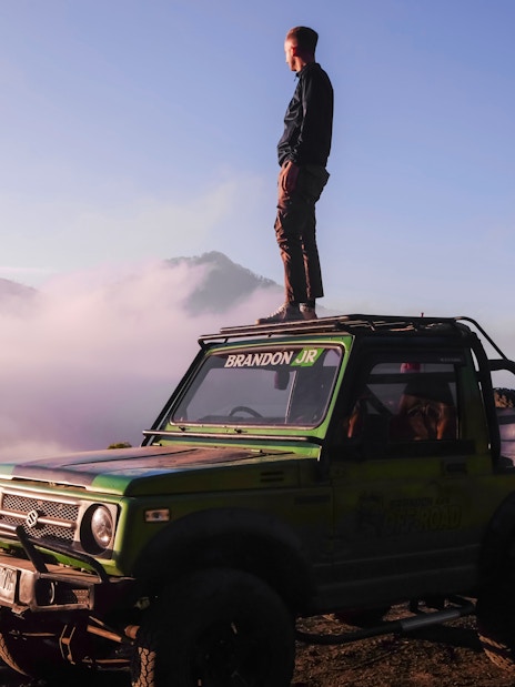 Man standing on a jeep during Black Lava Exploration in Bali with misty mountains in the background.
