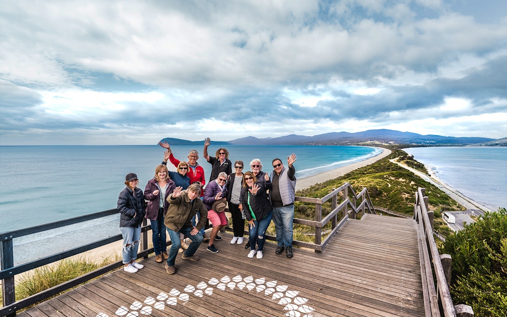 Group of people waving on a boardwalk overlooking Bruny Island coastline, Hobart.