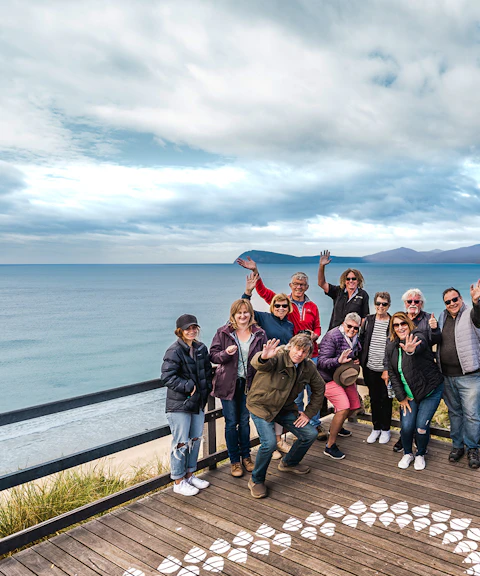 Group of people waving on a boardwalk overlooking Bruny Island coastline, Hobart.