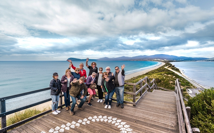 Group of people waving on a boardwalk overlooking Bruny Island coastline, Hobart.