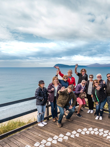 Group of people waving on a boardwalk overlooking Bruny Island coastline, Hobart.