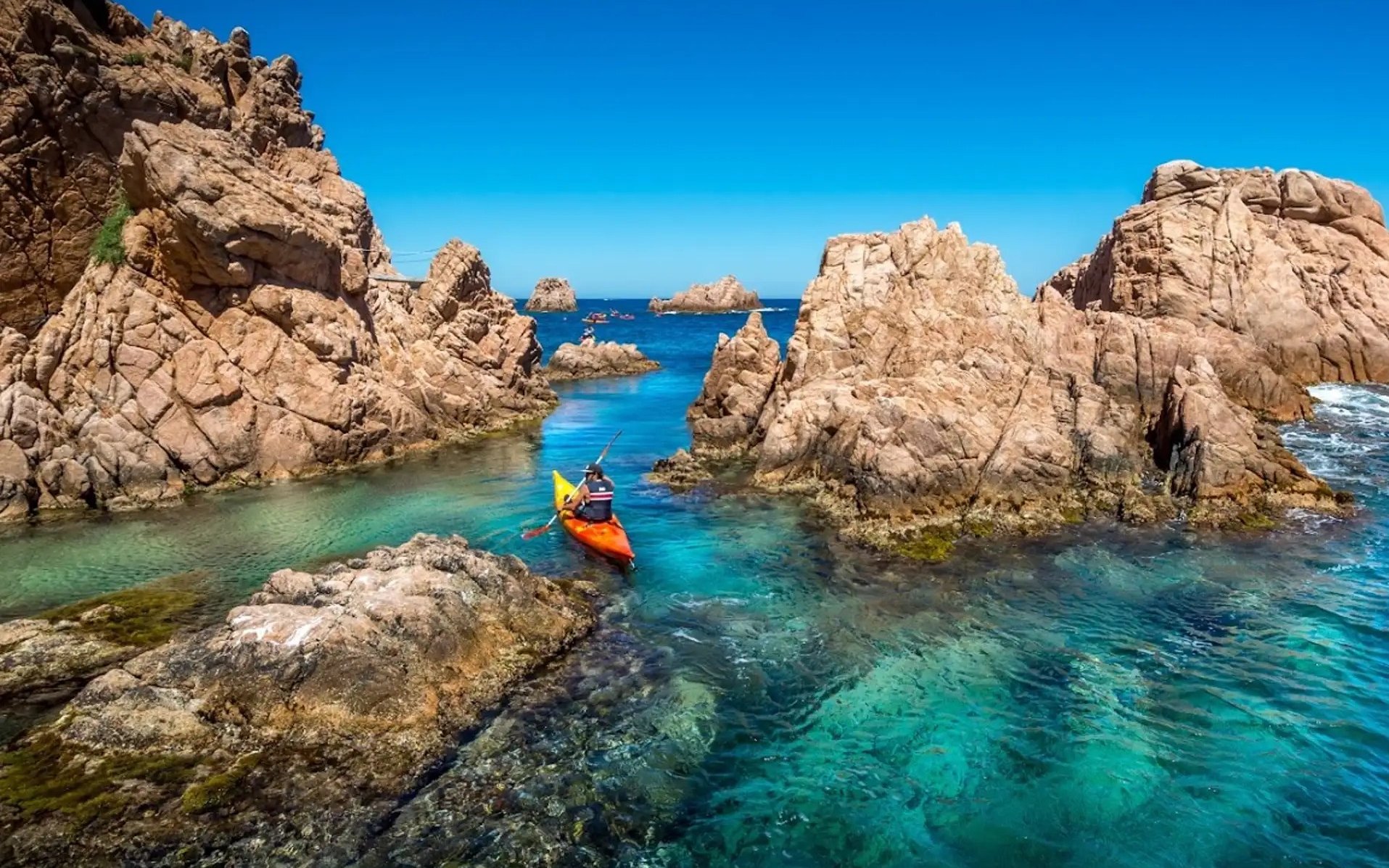 Visitors kayaking through rocky waters at Costa Brava.