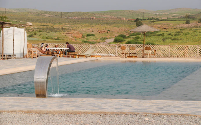 Poolside dining area with people seated, overlooking Agafay desert landscape.
