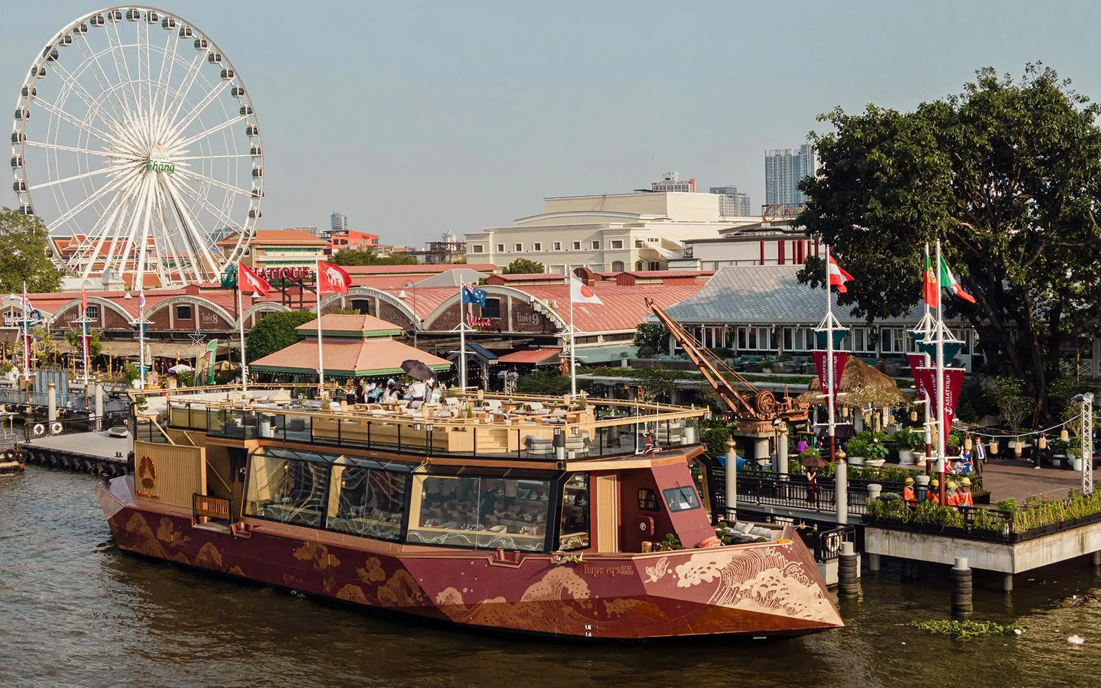 Okura Cruise boat docked at Asiatique Riverfront with Ferris wheel in Bangkok.