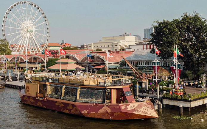 Okura Cruise boat docked at Asiatique Riverfront with Ferris wheel in Bangkok.