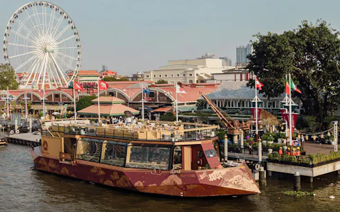 Okura Cruise boat docked at Asiatique Riverfront with Ferris wheel in Bangkok.
