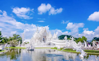 White Temple (Wat Rong Khun) exterior with intricate sculptures and reflection in pond, Chiang Rai, Thailand.