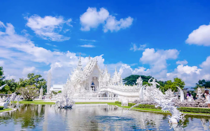 White Temple (Wat Rong Khun) exterior with intricate sculptures and reflection in pond, Chiang Rai, Thailand.