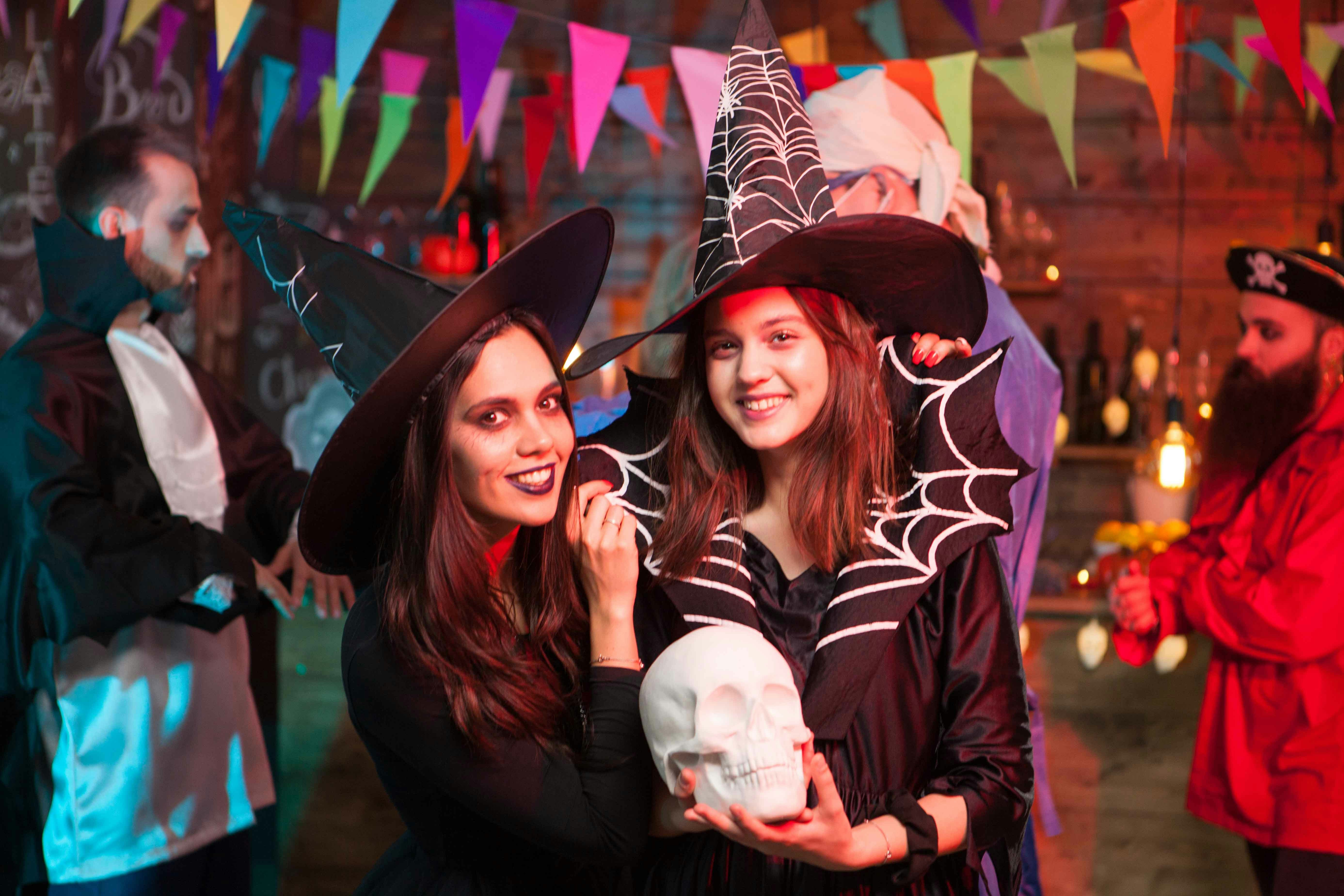 Witches in costumes holding a skull at a Halloween party with colorful flags.