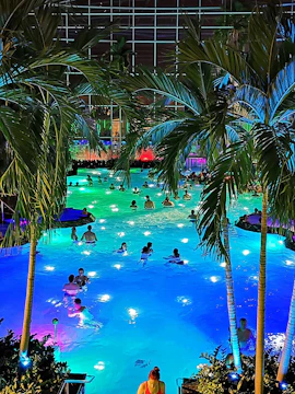 People enjoying a colorful indoor pool at Therme Bucuresti, surrounded by palm trees.