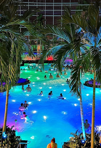 People enjoying a colorful indoor pool at Therme Bucuresti, surrounded by palm trees.