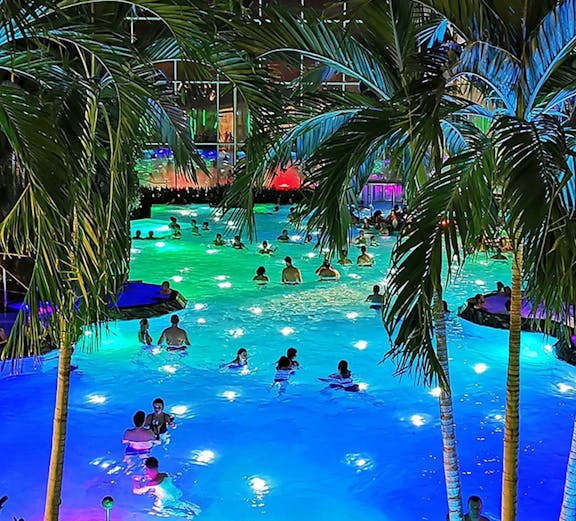 People enjoying a colorful indoor pool at Therme Bucuresti, surrounded by palm trees.