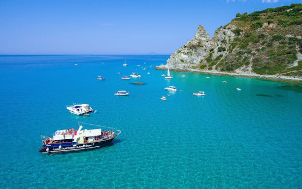 Boat trip near Capo Vaticano cliffs, Tropea, with several boats on clear blue water.