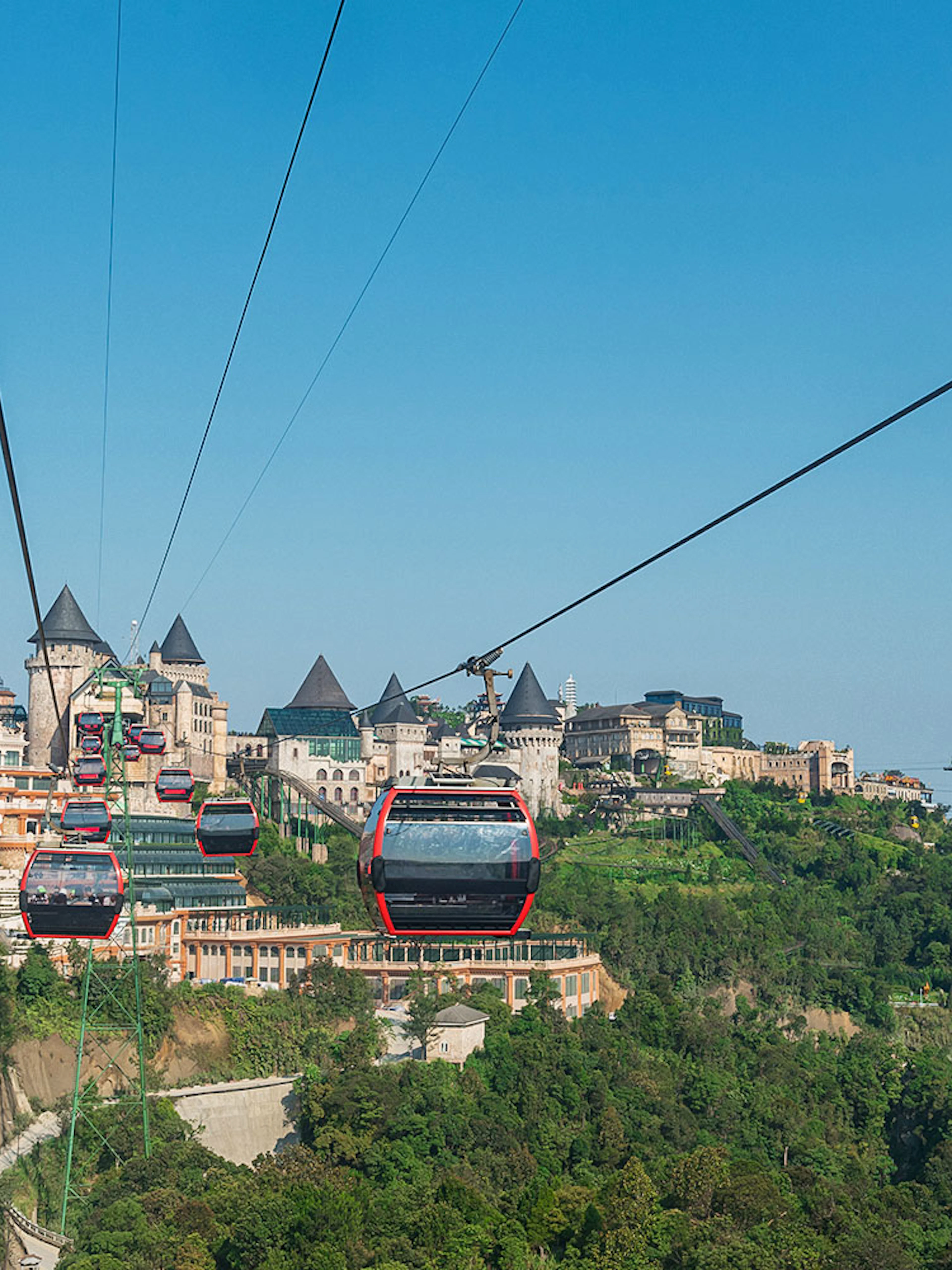 Cable cars traveling to Ba Na Hills in Da Nang, Vietnam with castle-like structures in view.