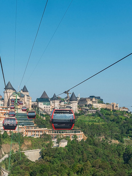 Cable cars traveling to Ba Na Hills in Da Nang, Vietnam with castle-like structures in view.