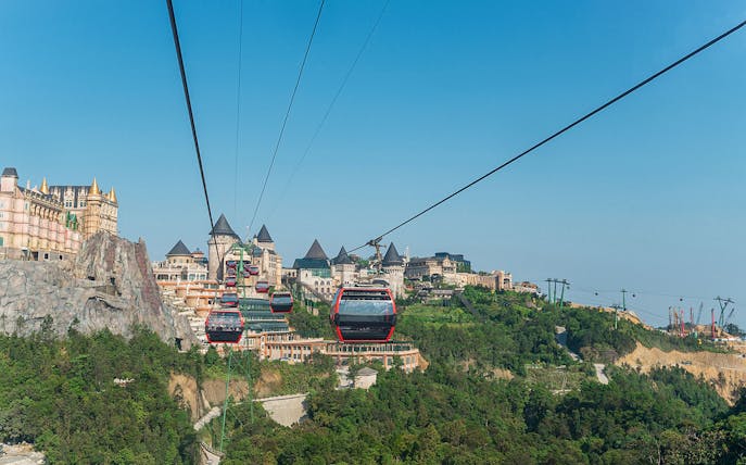 Cable cars traveling to Ba Na Hills in Da Nang, Vietnam with castle-like structures in view.