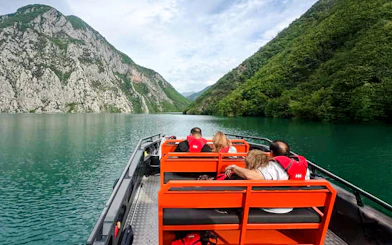 Boat tour on Komani Lake with passengers viewing lush mountains and clear water.