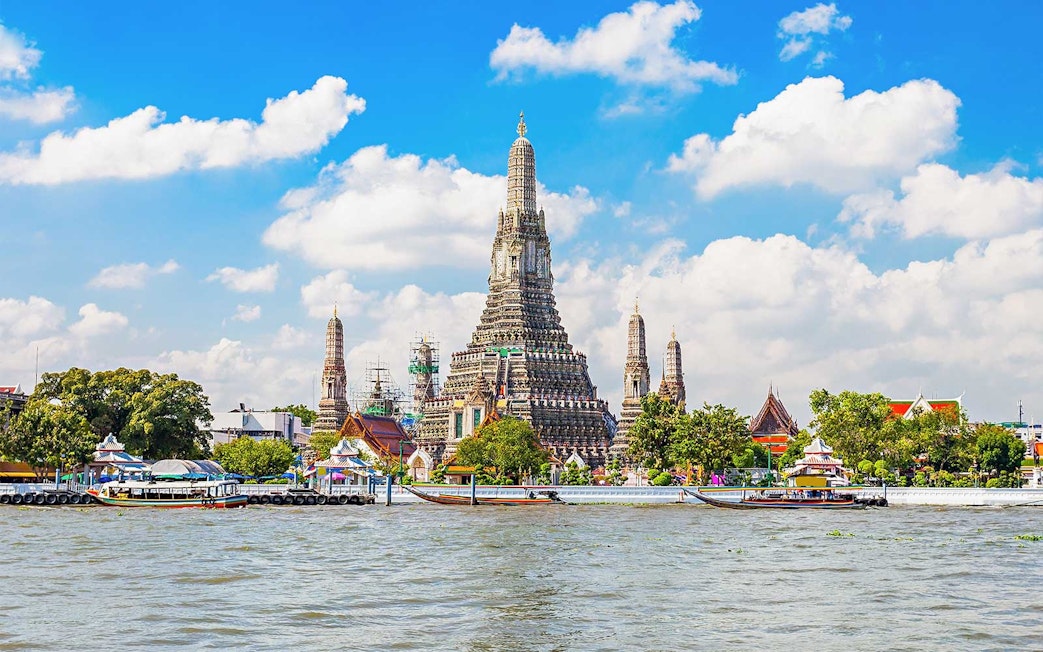 Wat Arun temple on Chao Phraya River, Bangkok, with boats in foreground.