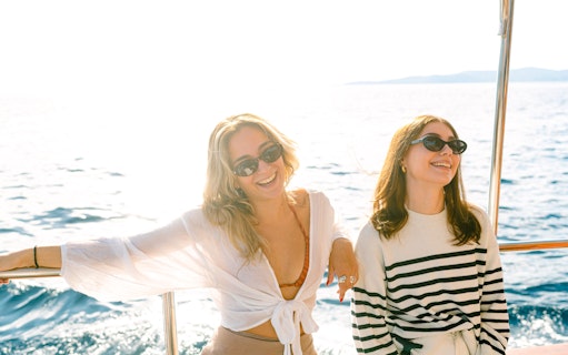 Two women smiling on a boat with ocean view in the background.
