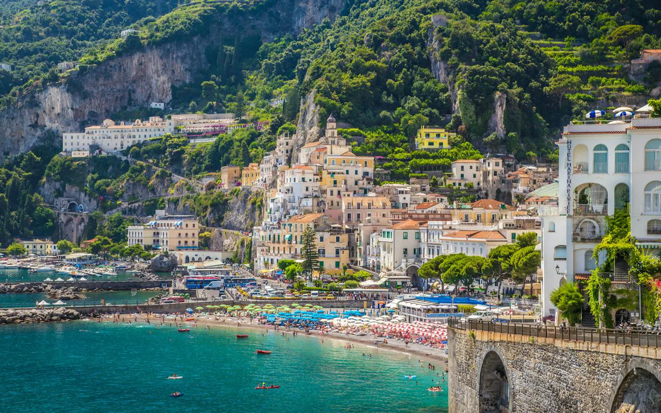 Amalfi coast view with colorful buildings, beach, and cliffs in Amalfi, Italy.