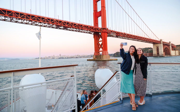 Guests taking a selfie on a San Francisco dinner cruise with Golden Gate Bridge in the background.