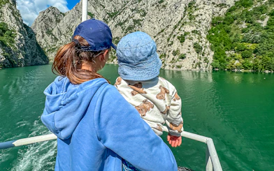 Mother and baby on ferry boat tour on Lake Komani, surrounded by rocky cliffs.