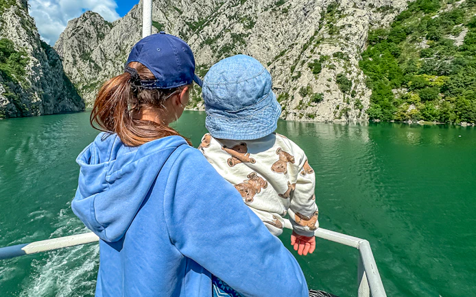 Mother and baby on ferry boat tour on Lake Komani, surrounded by rocky cliffs.