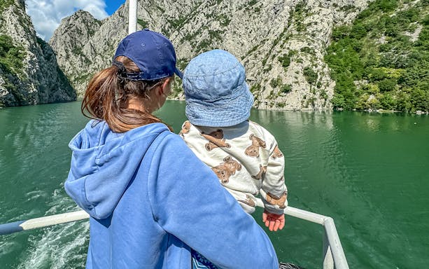 Mother and baby on ferry boat tour on Lake Komani, surrounded by rocky cliffs.